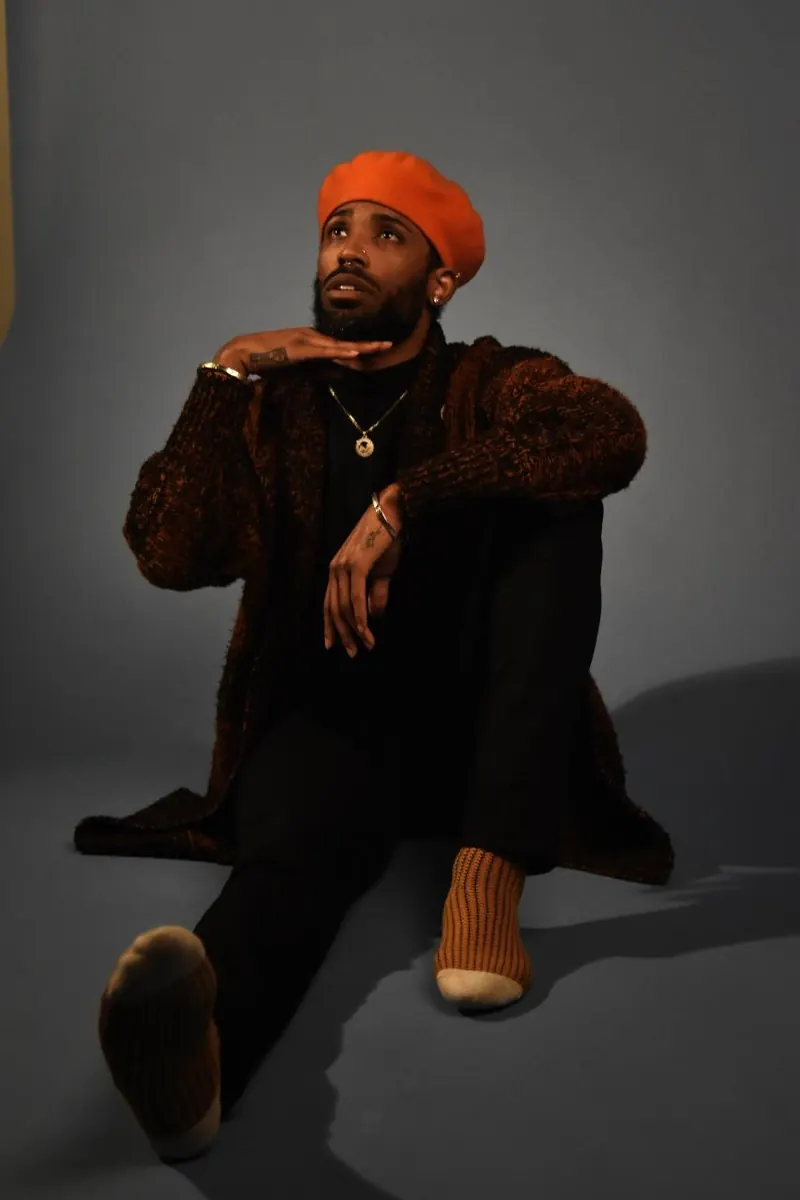 Studio portrait of a man in an orange beret, sitting on the floor and looking up