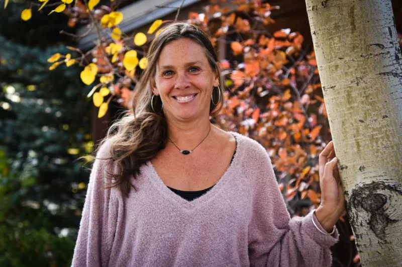 Smiling woman leaning on an aspen trunk with fall leaves behind her