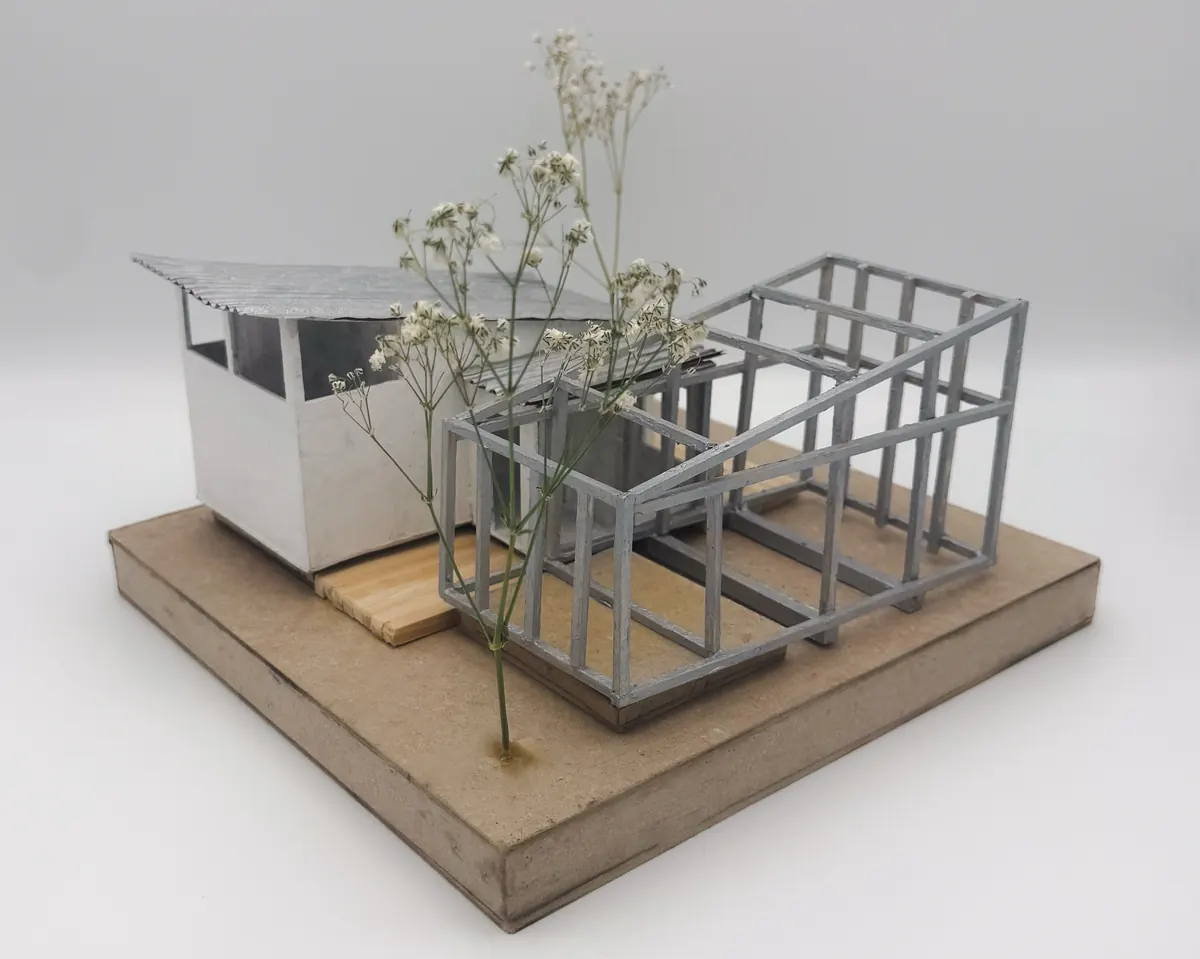 Architectural model of a white room beside an open gray frame, with dried flowers
